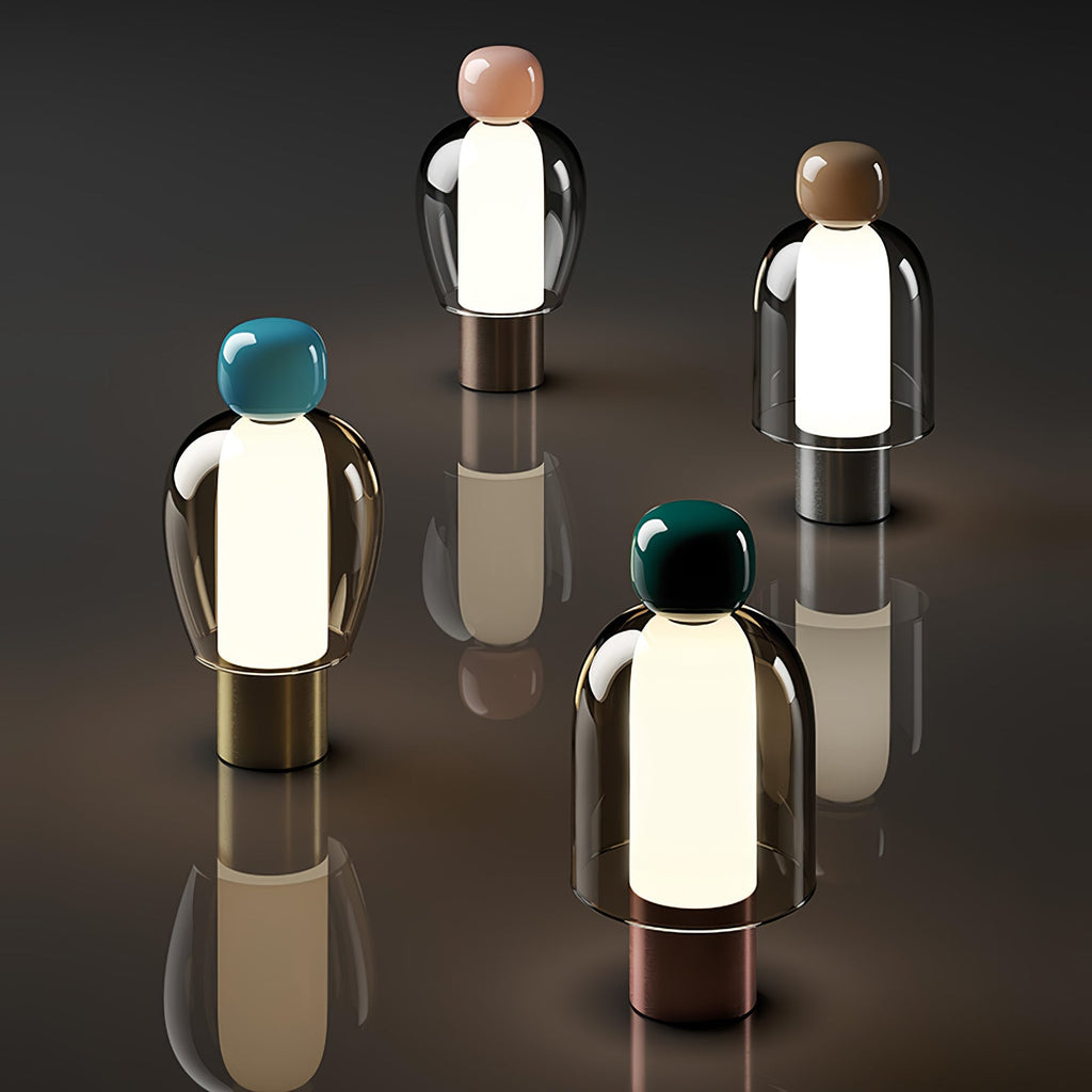 Four lit Clérachic table lamps with pink, brown, turquoise and dark green caps, standing apart on a dark reflective surface.