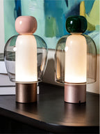 Close view of pink-capped and dark green-capped Clérachic table lamps, their glass domes lit warm, against a teal painting.