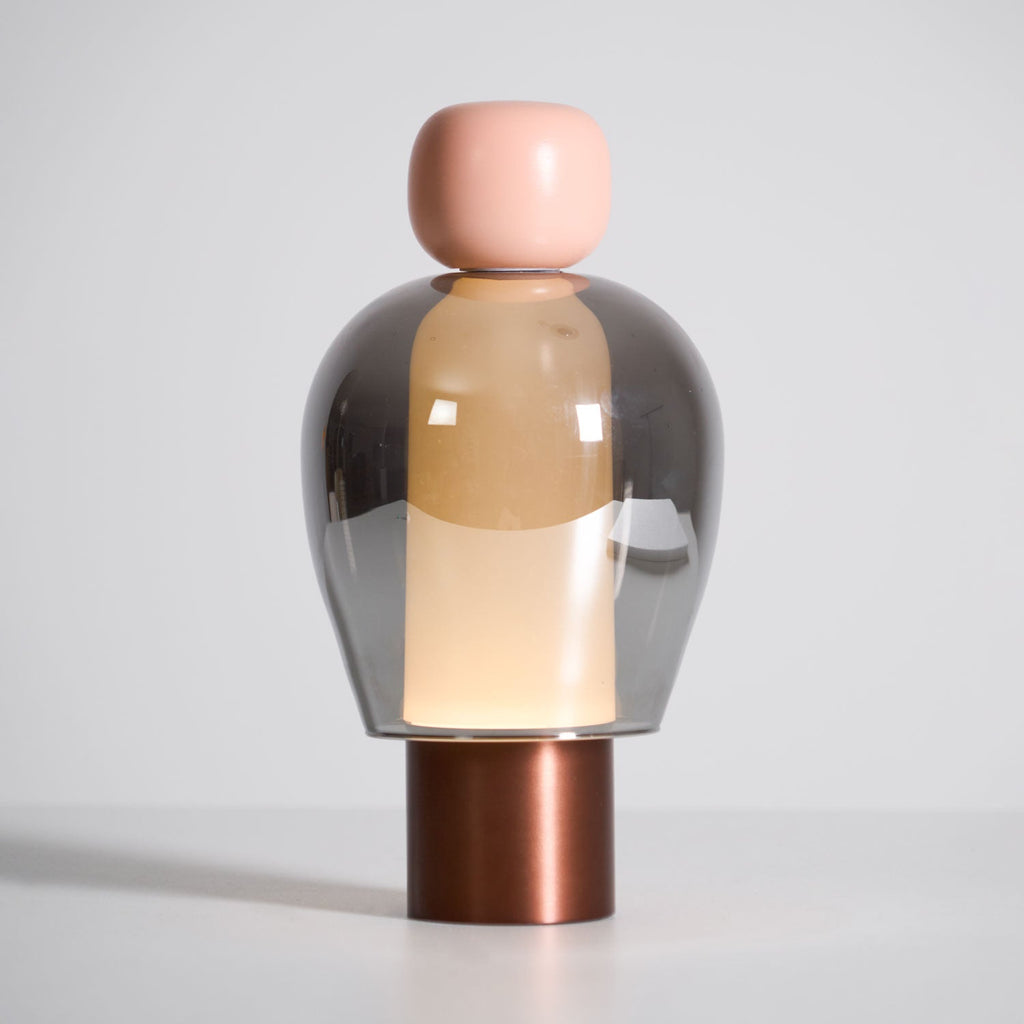 Front view of this Clérachic table lamp on a pale grey backdrop, a pink cap above a smoked glass dome and a copper-toned base.