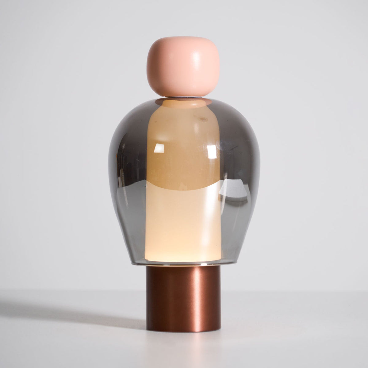Front view of this Clérachic table lamp on a pale grey backdrop, a pink cap above a smoked glass dome and a copper-toned base.