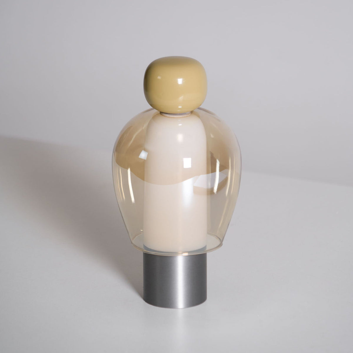 Close view of this Clérachic table lamp unlit, an olive cap above a cream inner column in an amber glass dome on a steel base.