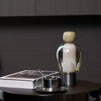 Near view of an olive-capped Clérachic table lamp beside a steel cup and a white book on a dark round table.