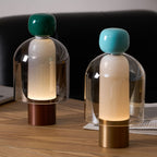 Close view of a dark green-capped and a turquoise-capped Clérachic table lamp on a wood desk, one with a copper and one with a brass base.