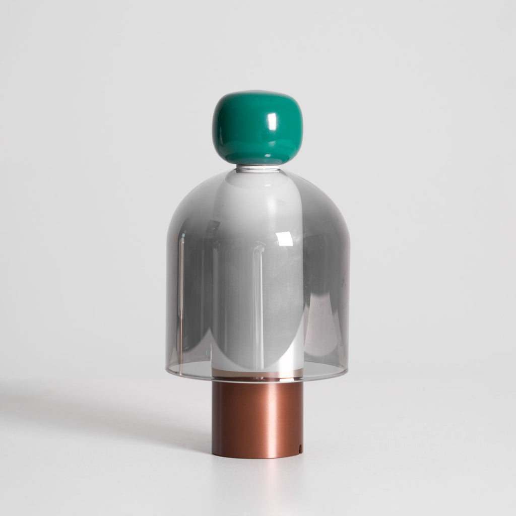 Front view of this Clérachic table lamp unlit on a pale backdrop, a green cap above a smoked grey glass dome and a copper-toned base.