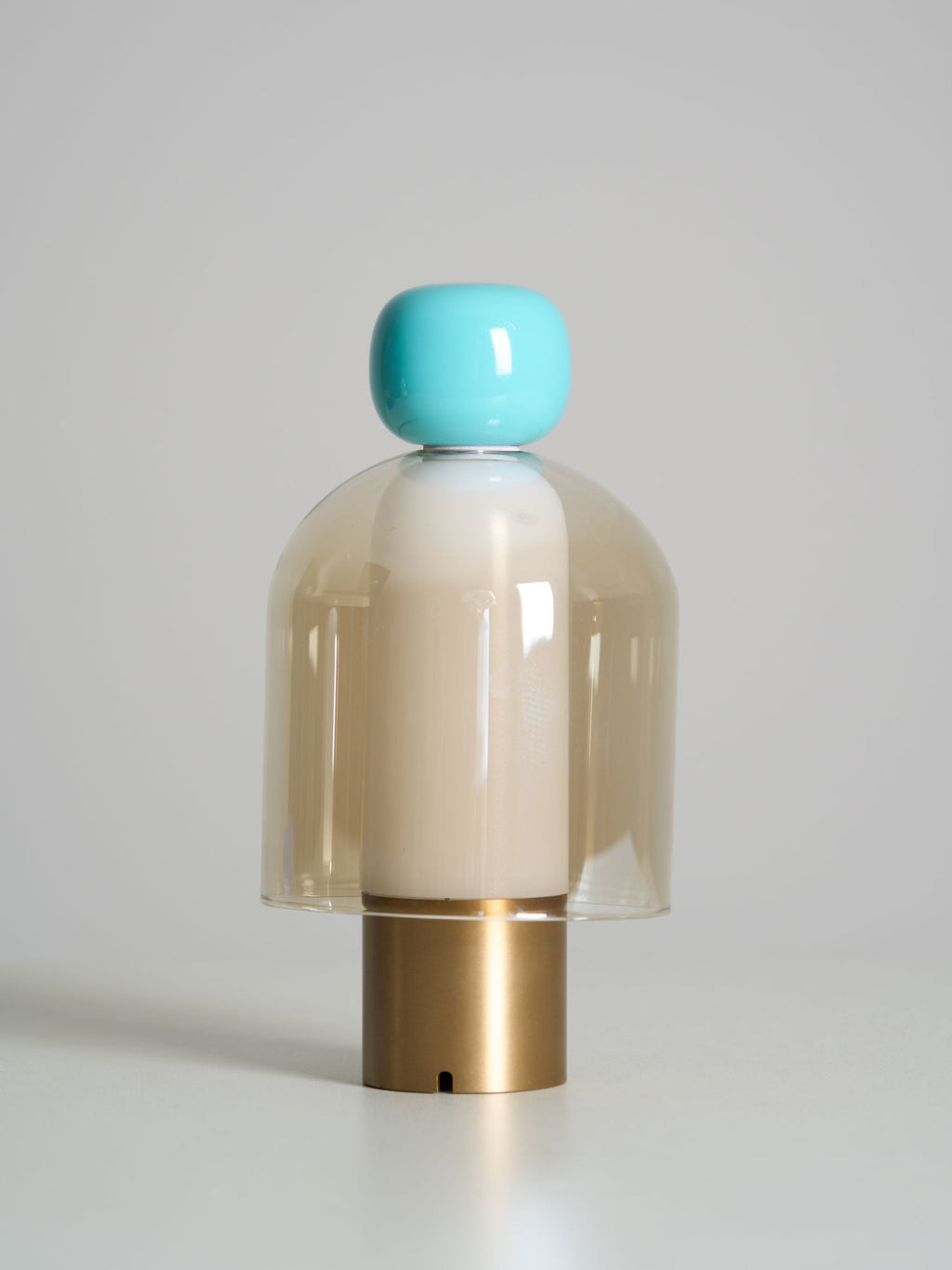 Unlit Clérachic table lamp with a turquoise cap, an amber glass dome and a brass base, on a soft grey background.