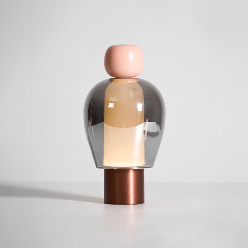 Pink-capped Clérachic table lamp on a white surface, a smoked glass dome over a glowing column and a copper-toned base.