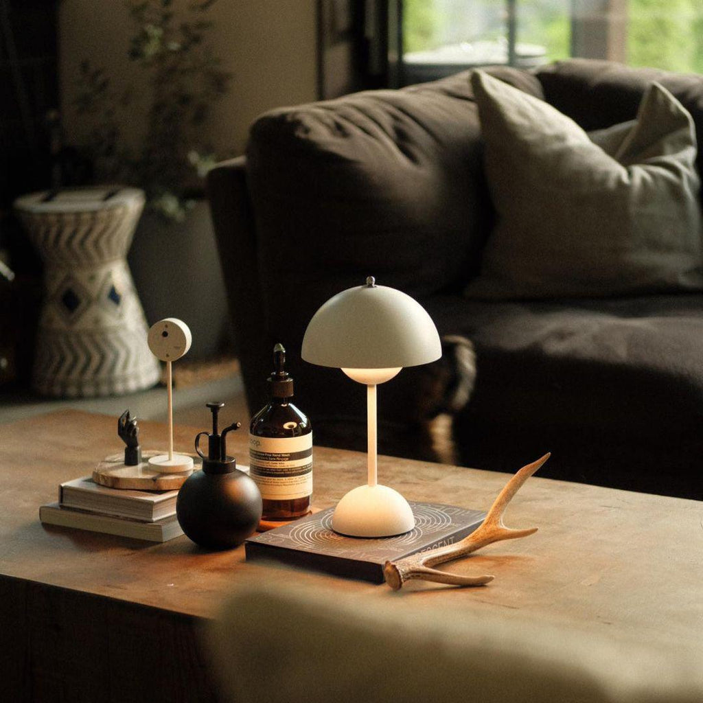 This Clérachic table lamp in cream sits on a wooden coffee table beside a dark glass bottle and a pair of antlers.