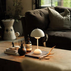 This Clérachic table lamp in cream sits on a wooden coffee table beside a dark glass bottle and a pair of antlers.