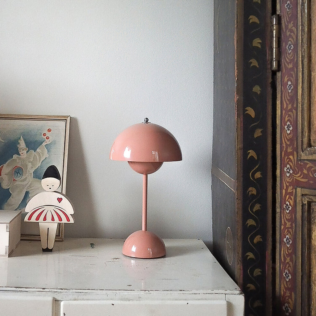A pink Clérachic table lamp on a white chest of drawers, with a small painted figure and a framed print behind it.
