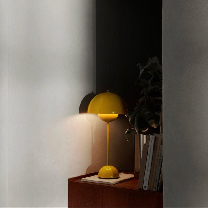 A yellow Clérachic table lamp throwing a warm pool of light onto the wall from a small wooden side table.