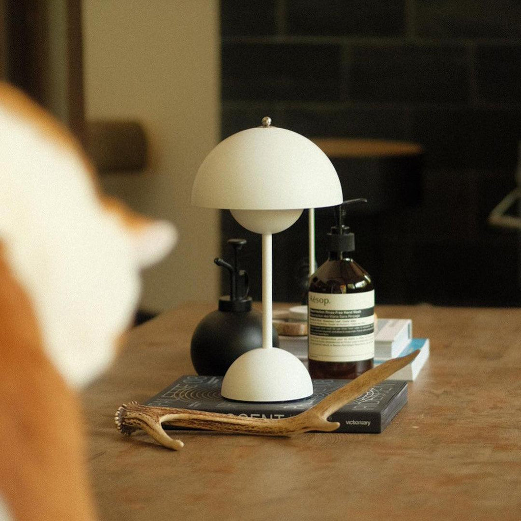 A cream Clérachic table lamp on a wooden table, with an amber bottle, a black vase and an antler nearby.