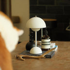 A cream Clérachic table lamp on a wooden table, with an amber bottle, a black vase and an antler nearby.