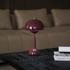A deep plum Clérachic table lamp on a dark patterned coffee table in front of a beige sofa, with magazines beside it.