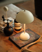 Close view of a cream Clérachic table lamp on a stack of books, with a small clock and a black bottle behind it.
