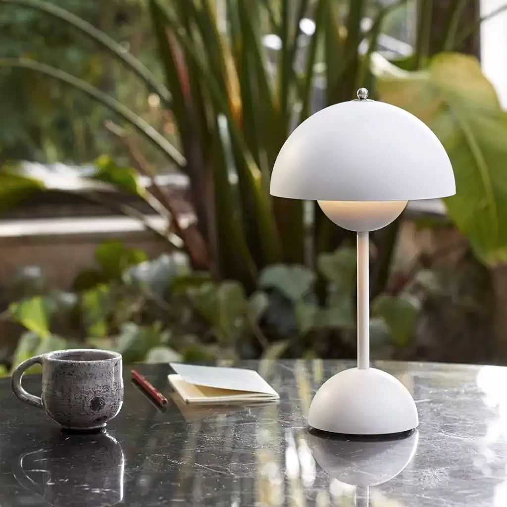 A white Clérachic table lamp on a dark marble table, with a stoneware mug and a notebook beside it.