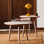 A small yellow Clérachic table lamp on a round wooden side table, with a magazine stack on the table in front.