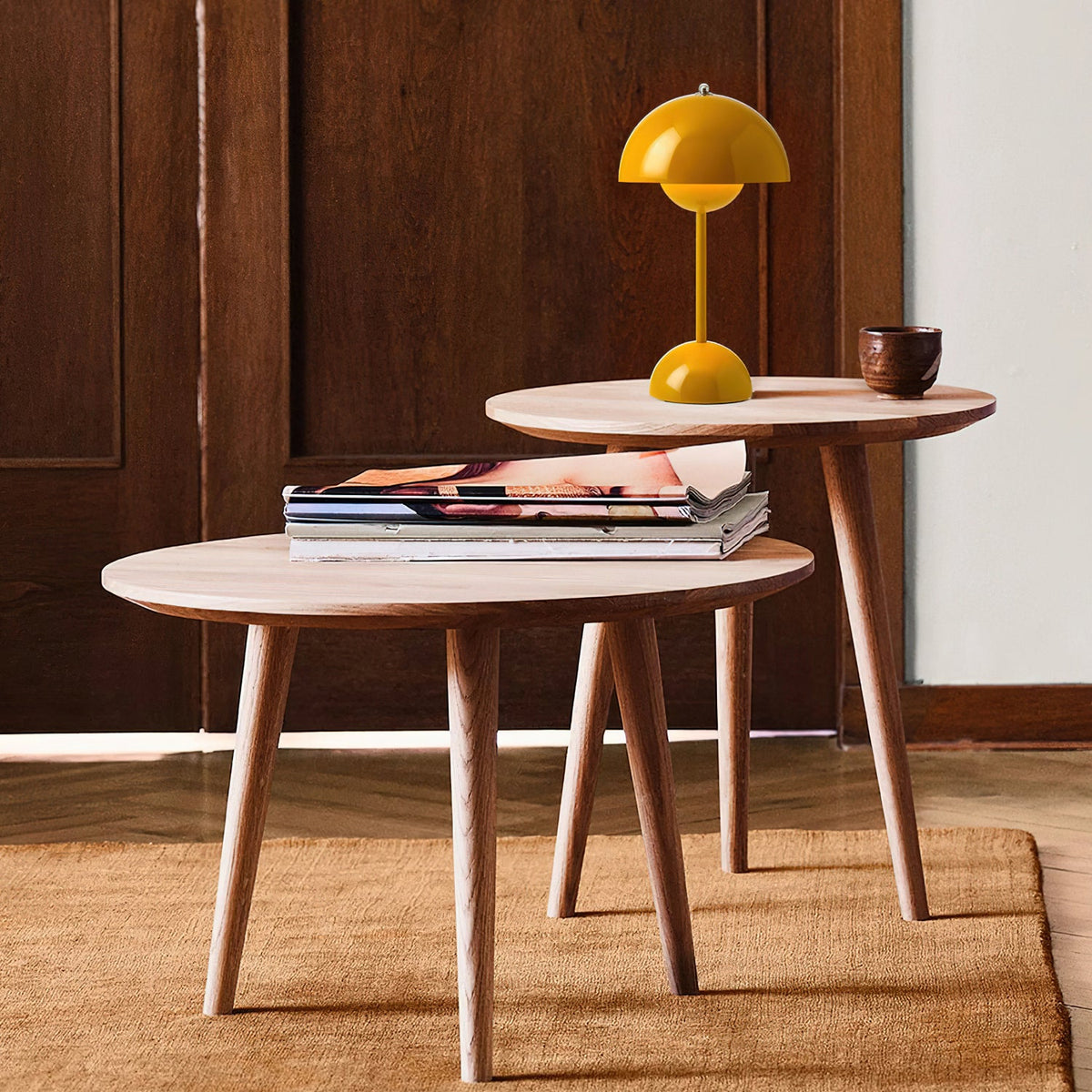 A small yellow Clérachic table lamp on a round wooden side table, with a magazine stack on the table in front.