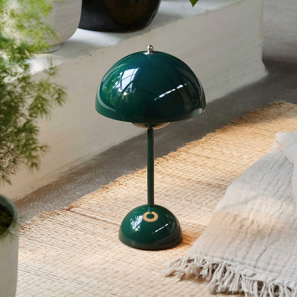 A dark-green Clérachic table lamp on a woven jute rug, beside a cream throw blanket and a leafy plant.
