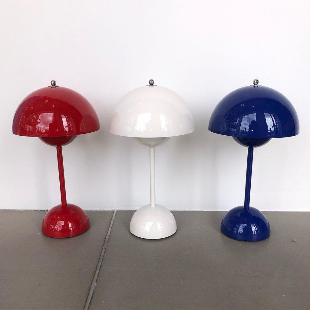 Three Clérachic table lamps in red, white and cobalt blue side by side on a grey floor against a white wall.