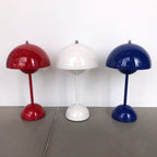 Three Clérachic table lamps in red, white and cobalt blue side by side on a grey floor against a white wall.
