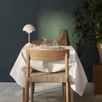 A small cream Clérachic table lamp on a laid dinner table with a white cloth, in front of a deep green wall.