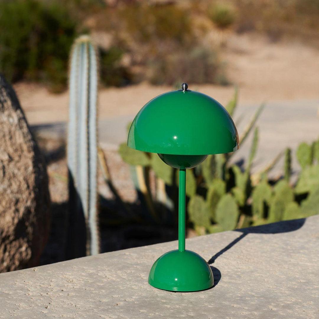 A bright green Clérachic table lamp on a stone ledge outdoors, with a tall cactus and dry hills behind.