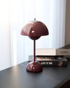 A deep plum Clérachic table lamp on a dark sideboard by a window, with a stack of books underneath its base.