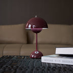 A deep plum Clérachic table lamp on a dark textured table, with its touch spot at the base and a book at its side.