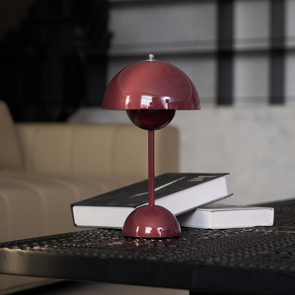 This Clérachic table lamp in burgundy with a dark book leaning against its base, in front of a beige sofa.