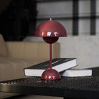 This Clérachic table lamp in burgundy with a dark book leaning against its base, in front of a beige sofa.