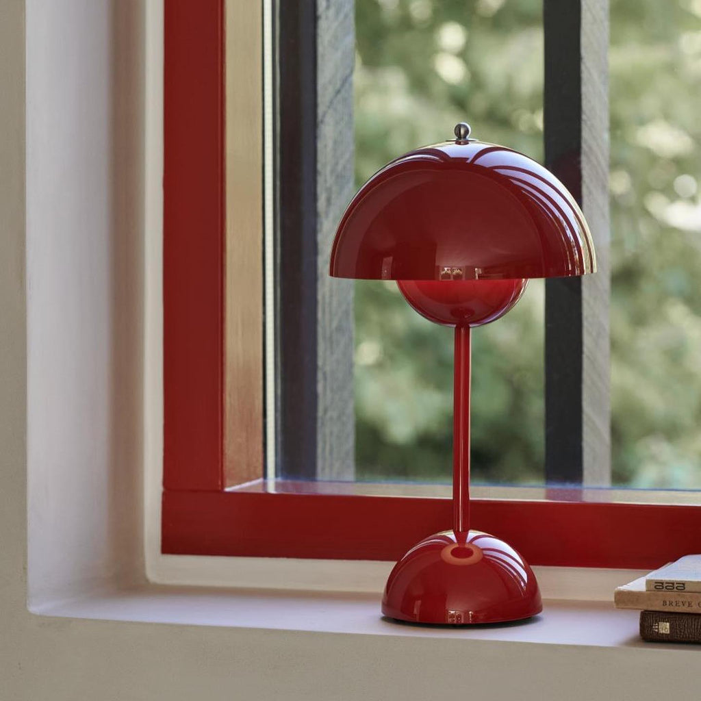 A red Clérachic table lamp on a deep window ledge with a red frame, and green trees visible outside.