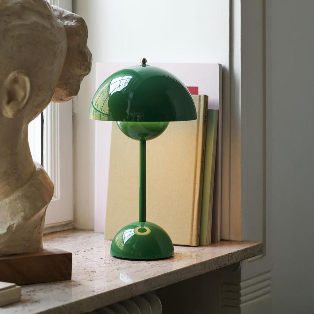A green Clérachic table lamp on a marble windowsill beside a row of books and a plaster bust.