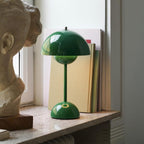 A green Clérachic table lamp on a marble windowsill beside a row of books and a plaster bust.