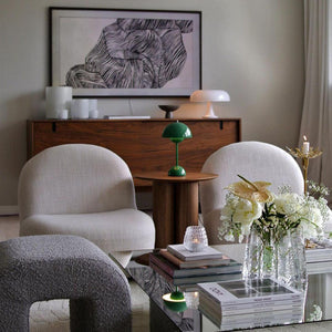 A small green Clérachic table lamp on a round table in a living room with cream armchairs, on a white mount.