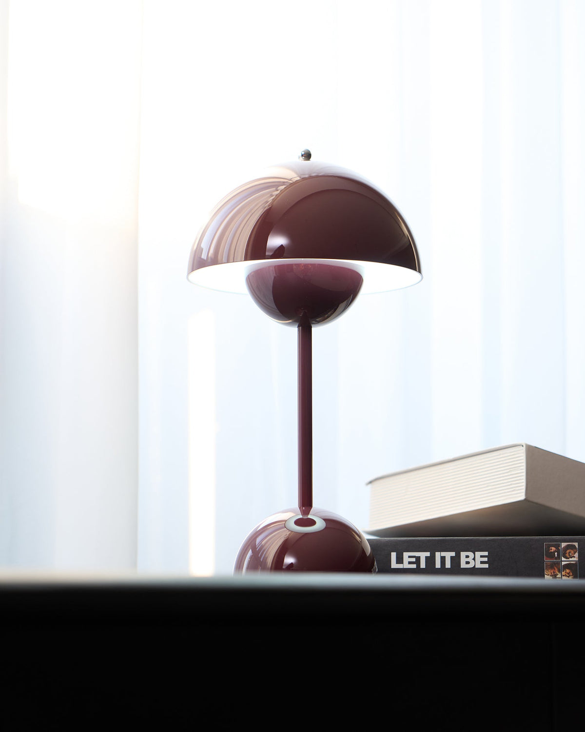 A deep plum Clérachic table lamp lit, with a bright rim under the shade, on a black desk beside books.