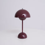 A deep plum Clérachic table lamp unlit, on a plain pale backdrop, showing its dome shade and rounded base.
