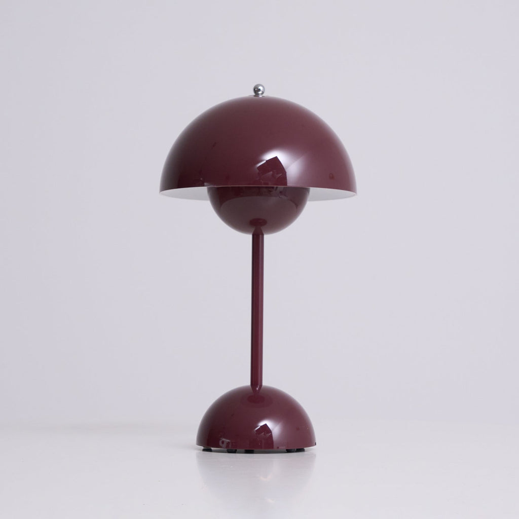 A deep plum Clérachic table lamp lit, with a bright rim under the shade, on a soft grey backdrop.