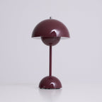 A deep plum Clérachic table lamp lit, with a bright rim under the shade, on a soft grey backdrop.