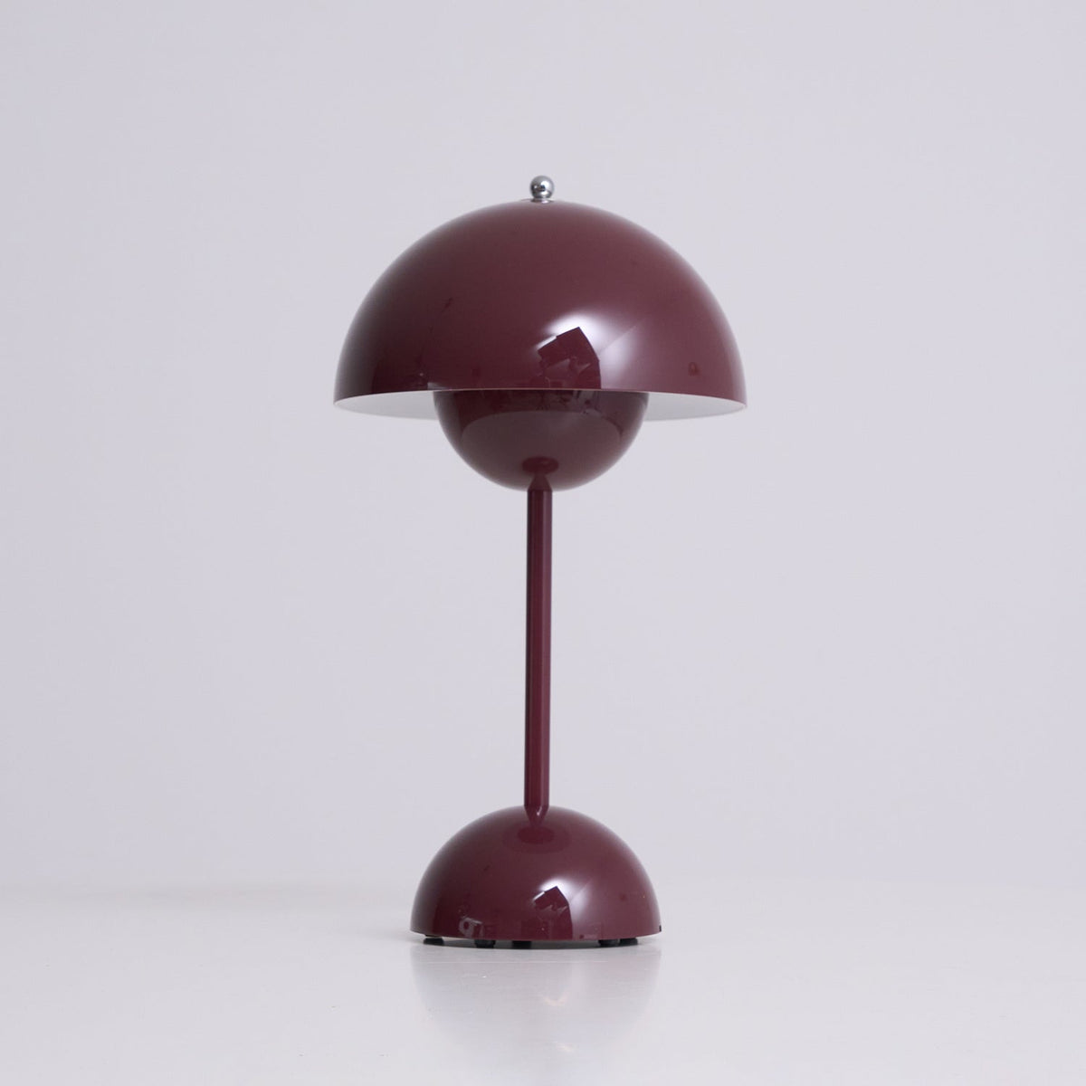 A deep plum Clérachic table lamp lit, with a bright rim under the shade, on a soft grey backdrop.