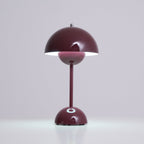 A deep plum Clérachic table lamp lit, with a white glow under the shade and a bright touch spot on the base.