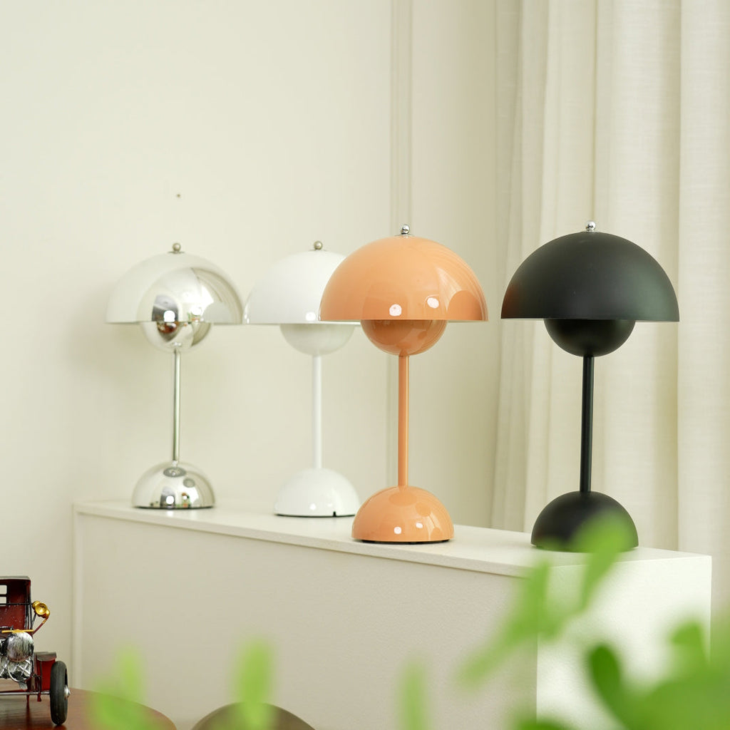 Four Clérachic table lamps in chrome, white, peach and black on a white shelf, in front of a cream curtain.