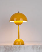 A yellow Clérachic table lamp lit, with a warm glow under the shade, on a rough pale stone ledge.