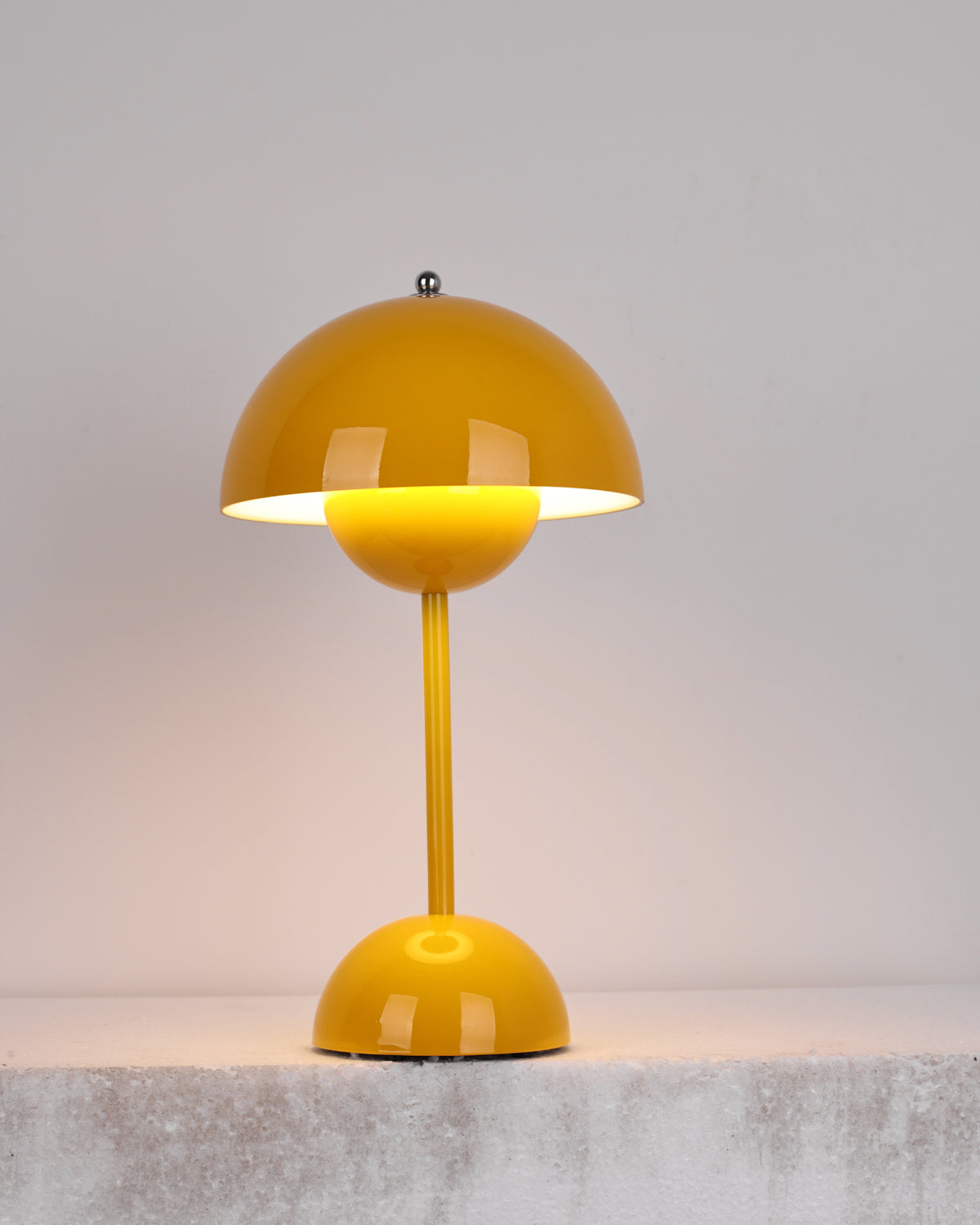 A yellow Clérachic table lamp lit, with a warm glow under the shade, on a rough pale stone ledge.