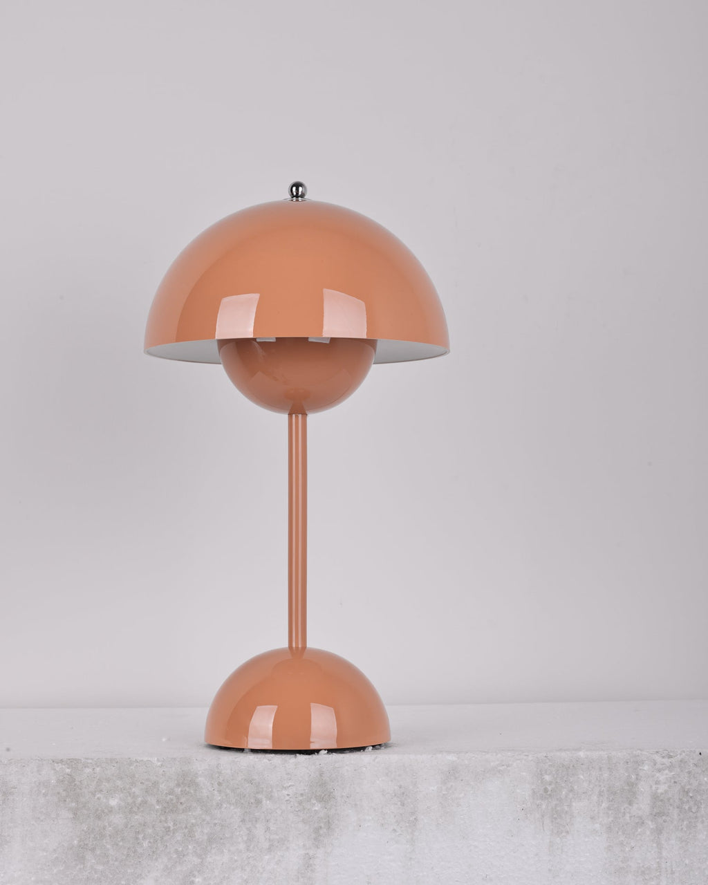 A peach-pink Clérachic table lamp unlit, on a soft grey backdrop above a rough pale ledge.
