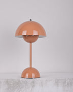 A peach-pink Clérachic table lamp unlit, on a soft grey backdrop above a rough pale ledge.