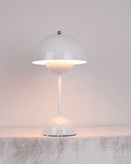 A white Clérachic table lamp lit, with a warm glow below the shade, on a rough pale stone ledge.