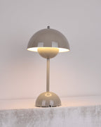 A grey Clérachic table lamp lit, with a warm glow below the shade, on a rough pale stone ledge.