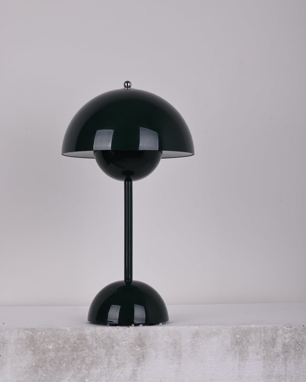 A dark-green Clérachic table lamp unlit, on a pale stone ledge against a soft grey backdrop.
