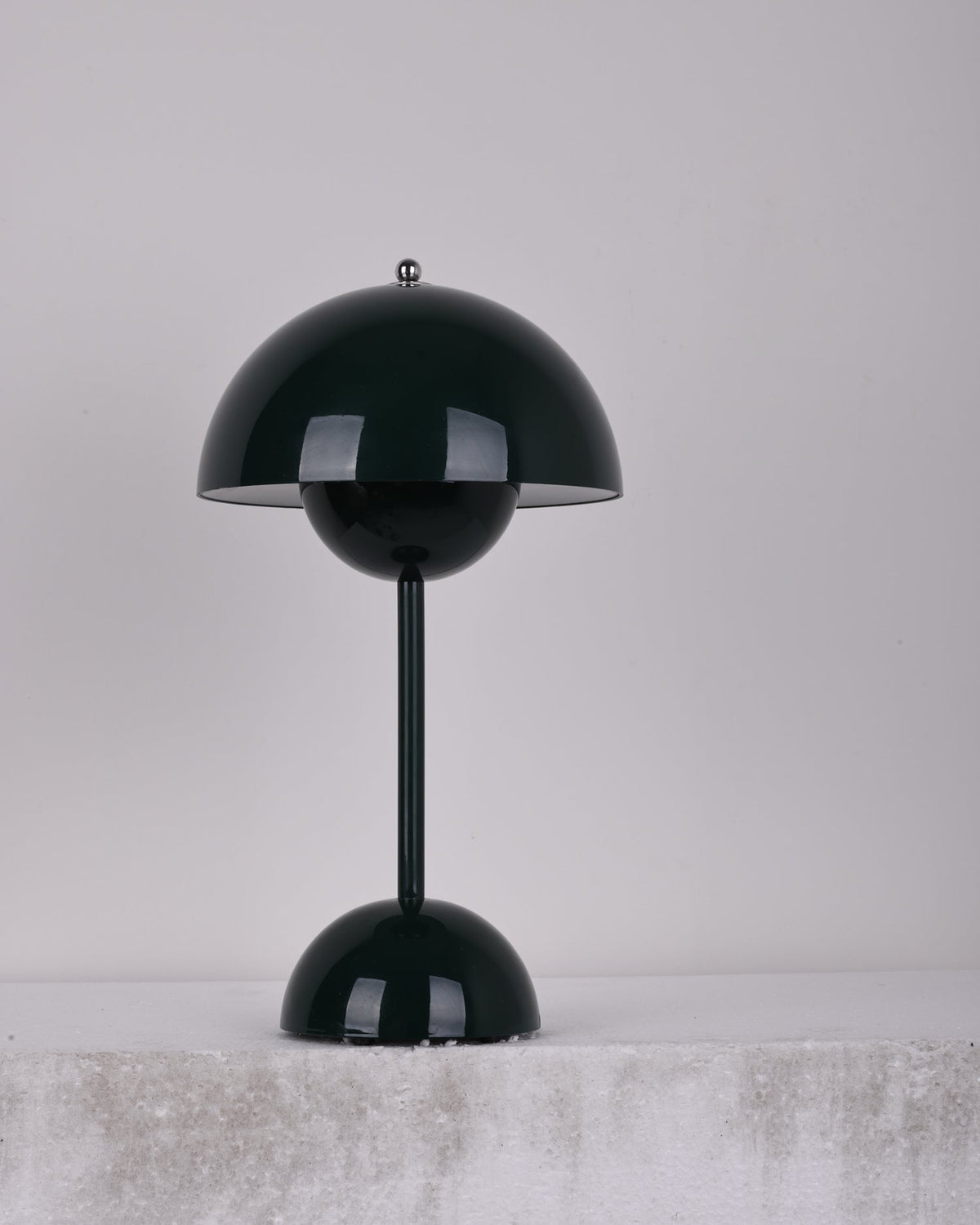 A dark-green Clérachic table lamp unlit, on a pale stone ledge against a soft grey backdrop.