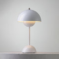 A white Clérachic table lamp lit, with a warm glow below the shade, on a pale stone ledge.